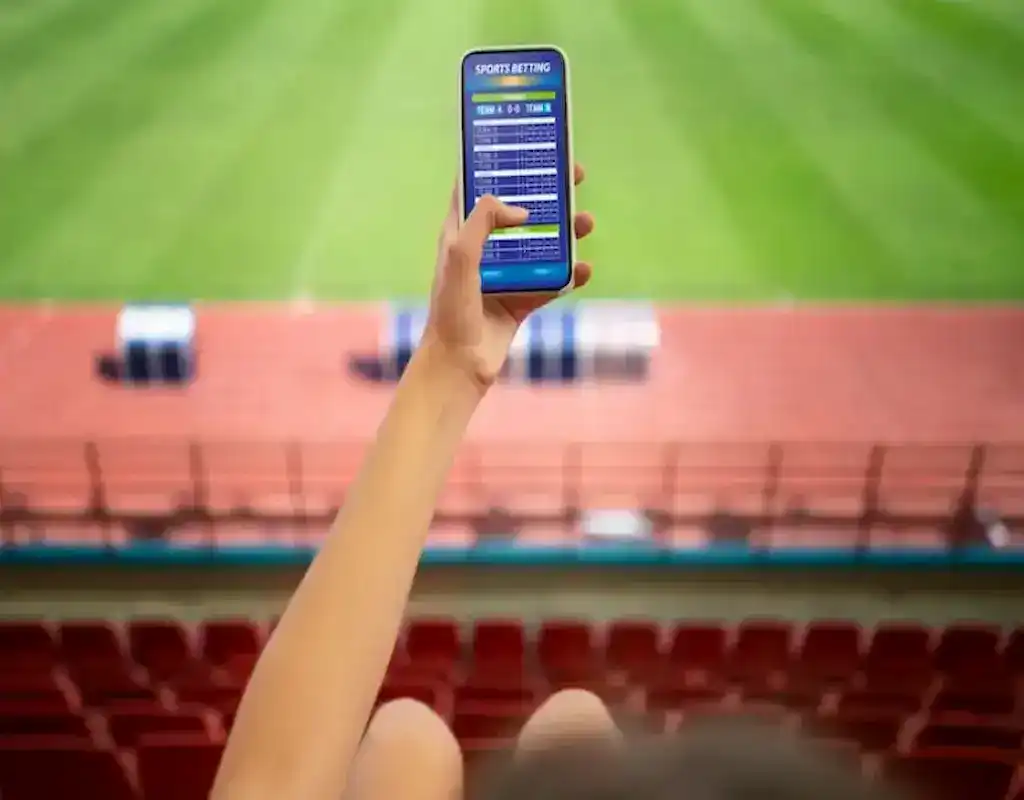 Person holding a smartphone showing sports betting odds while sitting in a stadium, representing online casino sign-up bonuses for sports bettors.